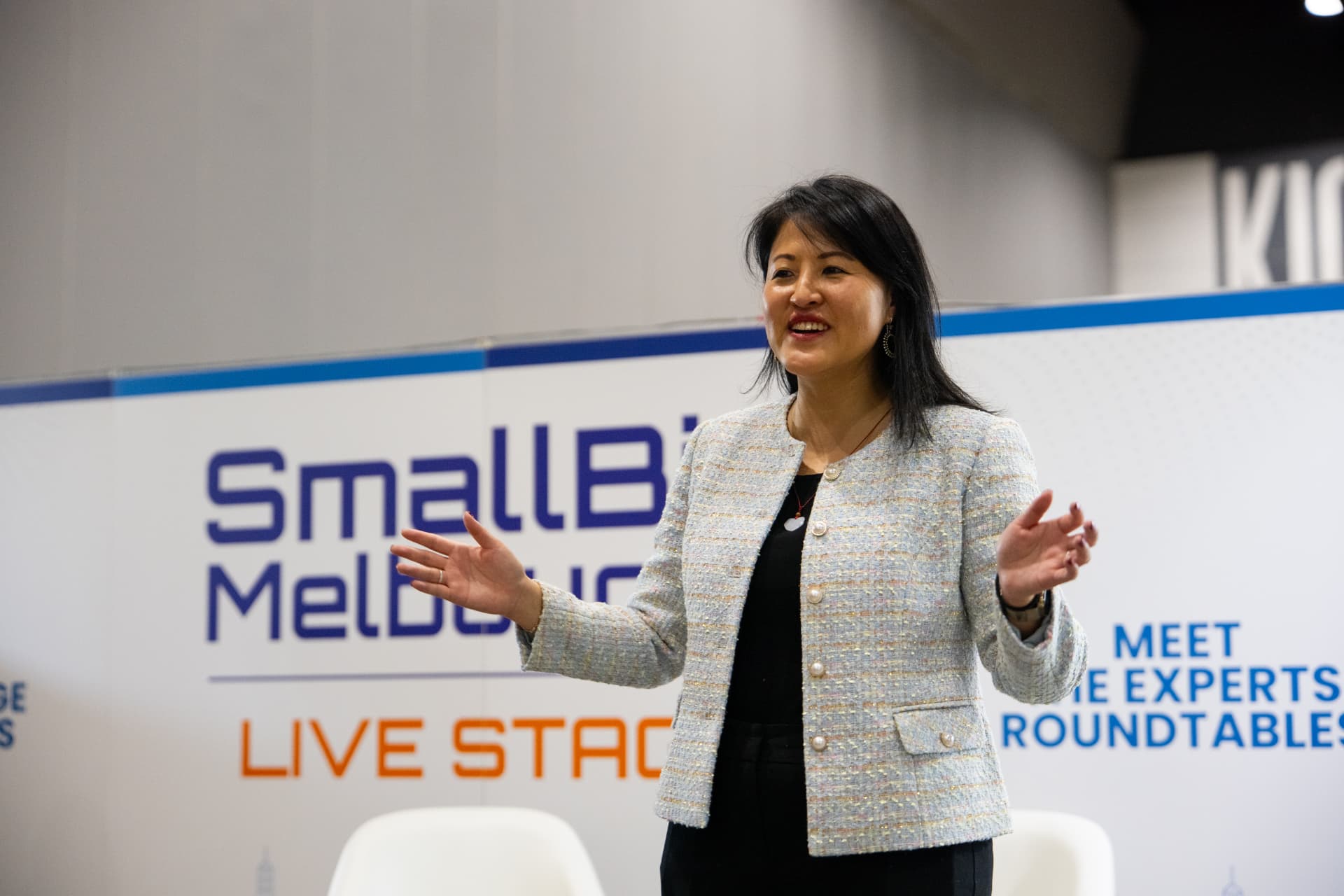 Lucy Lin speaking with open hands on the SmallBiz Melbourne live stage